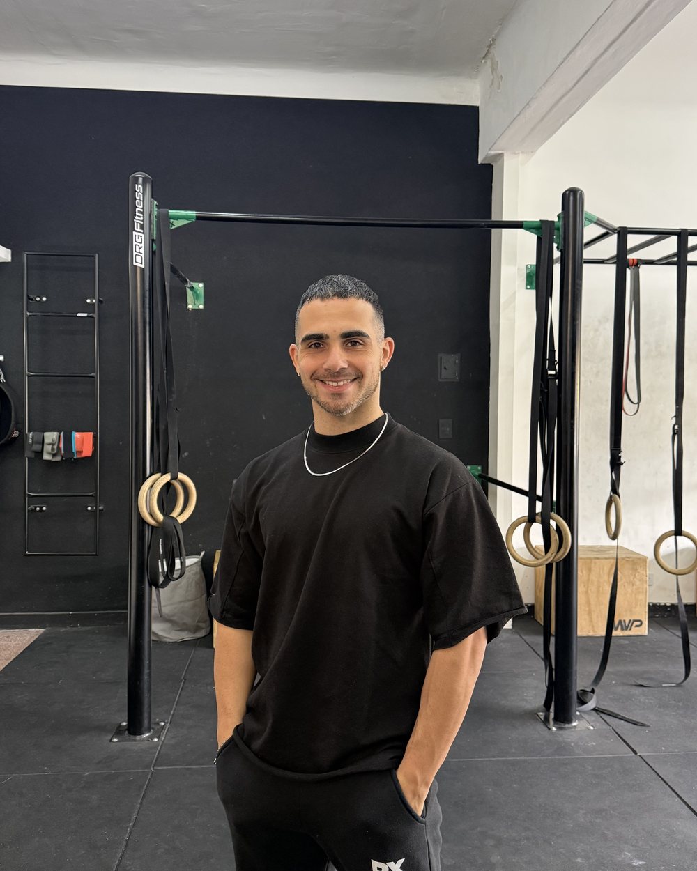 Axel Dominguez sonriendo en su gimnasio, con las manos en los bolsillos